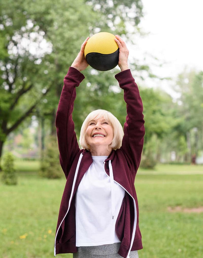 elderly sportswoman exercising with medicine ball in green park